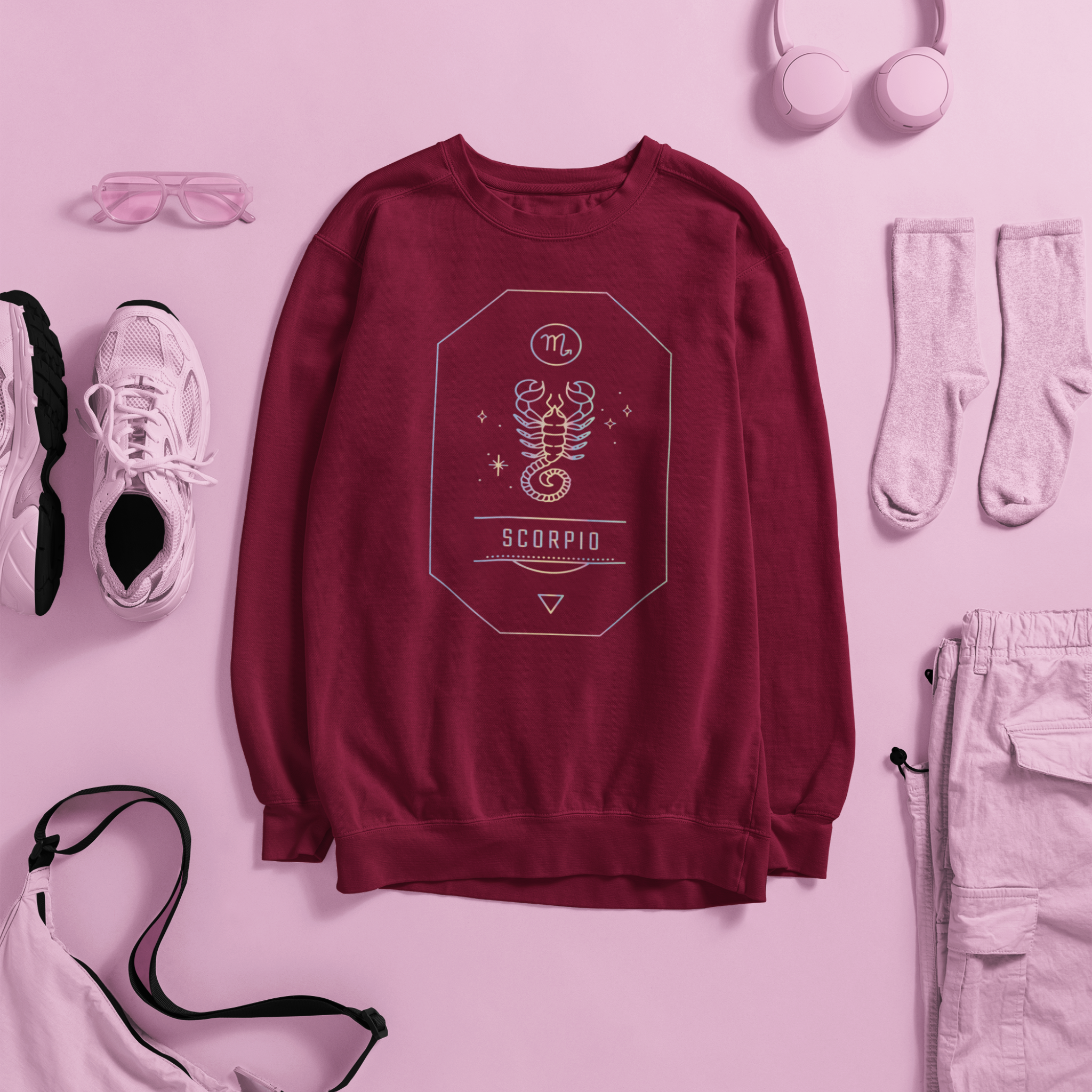 Maroon sweatshirt with Scorpio zodiac design on a pink background with accessories.