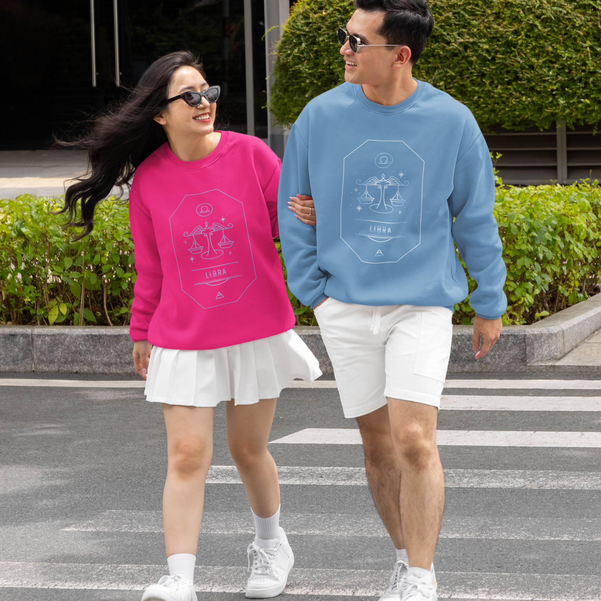 Two people walking on a street, wearing matching sweatshirts with the Libra zodiac sign.